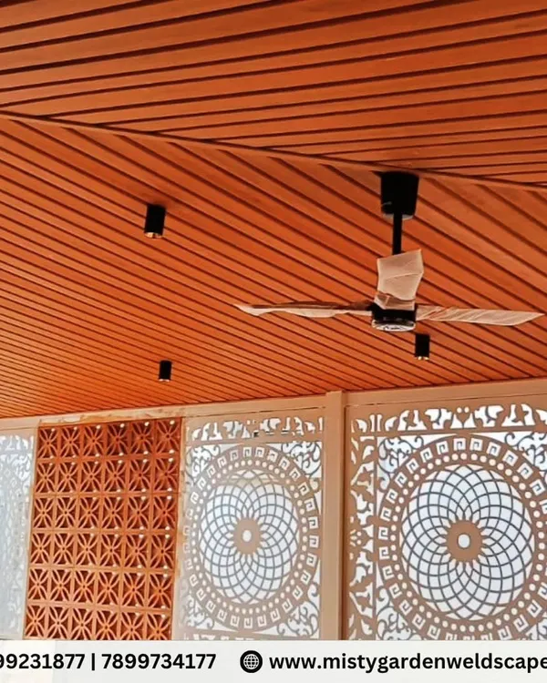 A stunning view of a completed terrace room featuring a combination of intricate white CNC panels and classic red jali bricks. The warm wood-finish PVC ceiling adds to the luxurious feel of this beautifully designed space.
