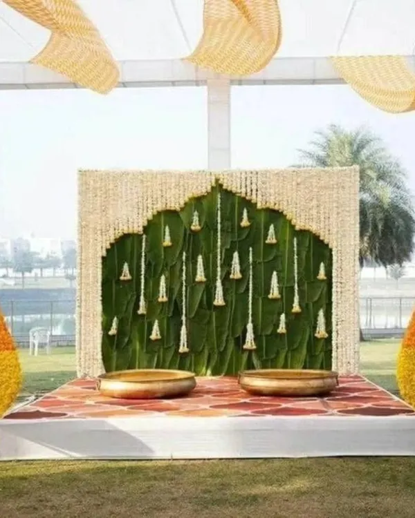 This stunning outdoor Haldi mandap is inspired by South Indian temple architecture, using a banana leaf wall and a floral arch to create a sacred and beautiful space.