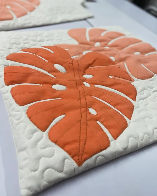 A close-up of a quilted cushion cover featuring a modern monstera leaf appliqué design with detailed stitching.