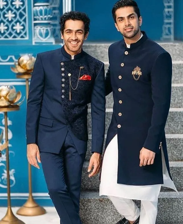 Two examples of our modern Indo-western designs. On the left, a navy blue Jodhpuri suit with a textured, darker blue waistcoat. On the right, a long navy bandhgala jacket with a gold brooch, worn over a white kurta.