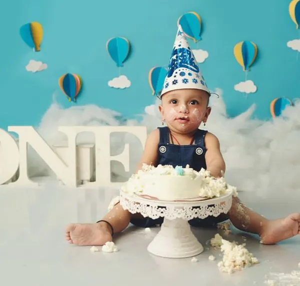 The aftermath of a successful cake smash. This little one is wearing a birthday hat and a face full of frosting, a perfect memory of his first birthday.