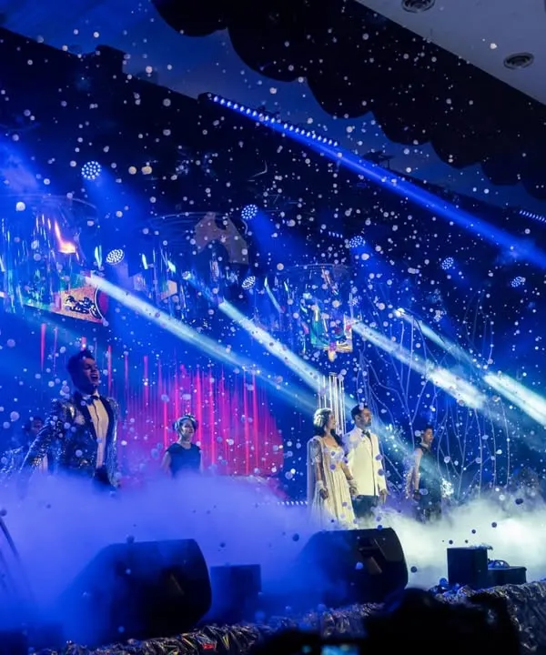 A high-energy moment on the Sangeet stage, captured with dramatic blue lighting, smoke effects, and a shower of confetti. We design the entire production to make family performances feel like a professional show.