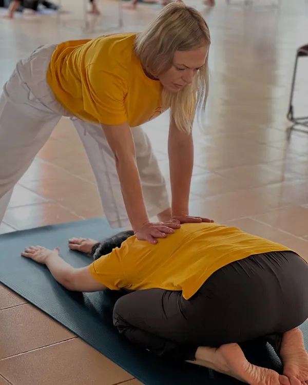 A teacher provides a gentle adjustment in Balasana (Child's Pose), helping the student release tension in the back and shoulders.