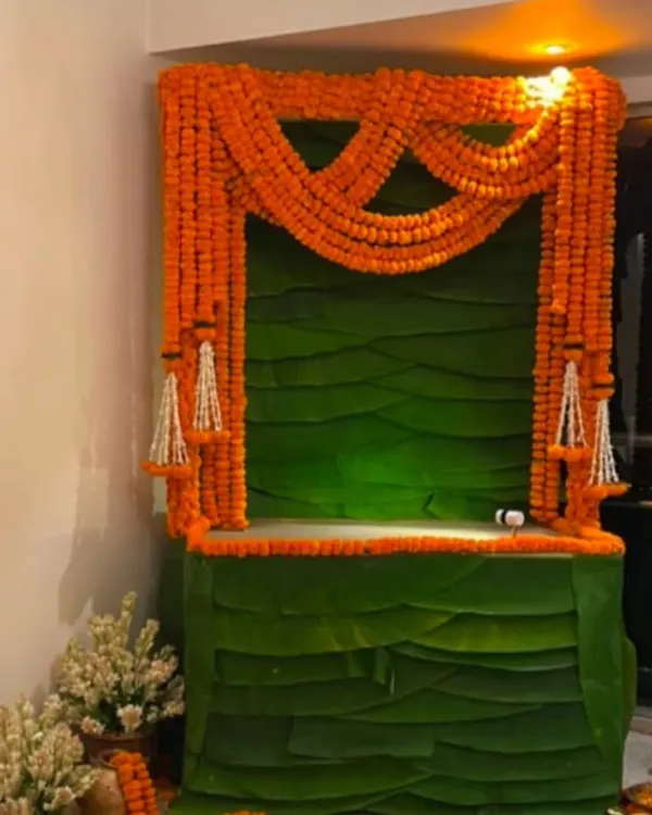 This is a classic South Indian inspired decor, featuring a structure made entirely of fresh banana leaves and draped with bright orange marigold garlands. It's a simple, elegant, and purely traditional way to set up your mandap.