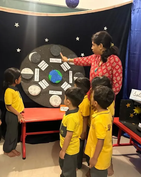 A teacher explains the phases of the moon to a group of curious students using a handmade model. We make astronomy accessible and fascinating, encouraging children to look up and wonder about the universe.