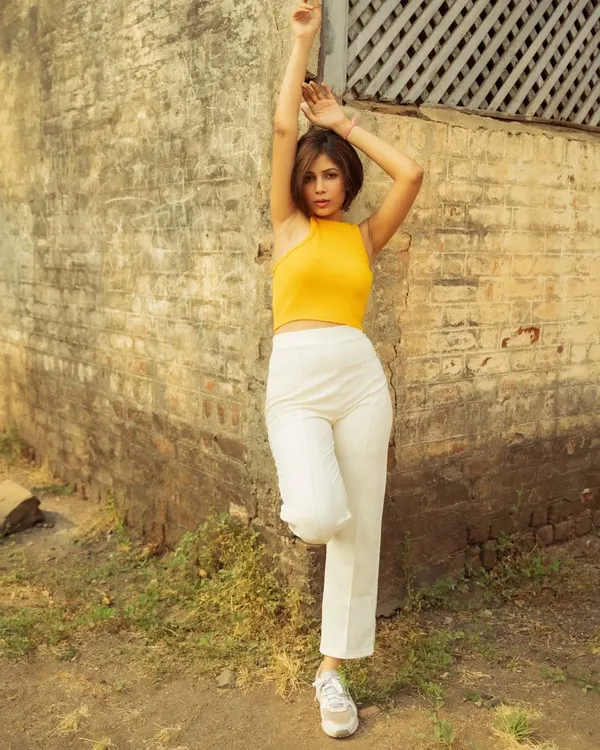 A fashion portrait taken during the golden hour against a rustic brick wall. The warm light on the model's yellow top creates a vibrant, eye-catching image.