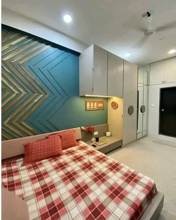 A bedroom interior featuring a unique chevron-patterned wooden headboard against a teal accent wall. The wardrobe and loft storage are seamlessly integrated for a clean finish.