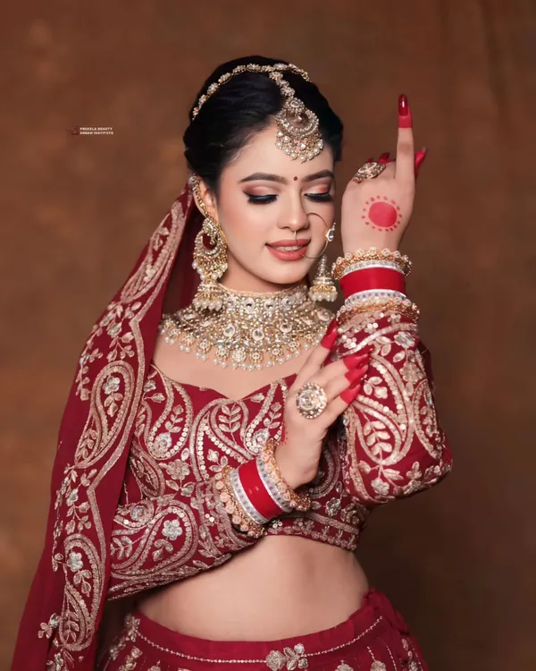 A picture of pure bridal grace. This look features a classic updo adorned with a white flower, paired with a stunning red lehenga and intricate jewelry, creating a timeless and regal wedding day aesthetic.