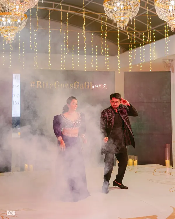 The couple's first dance at their Sangeet, surrounded by theatrical smoke. The decor features elegant chandeliers and fairy lights for a glamorous feel.