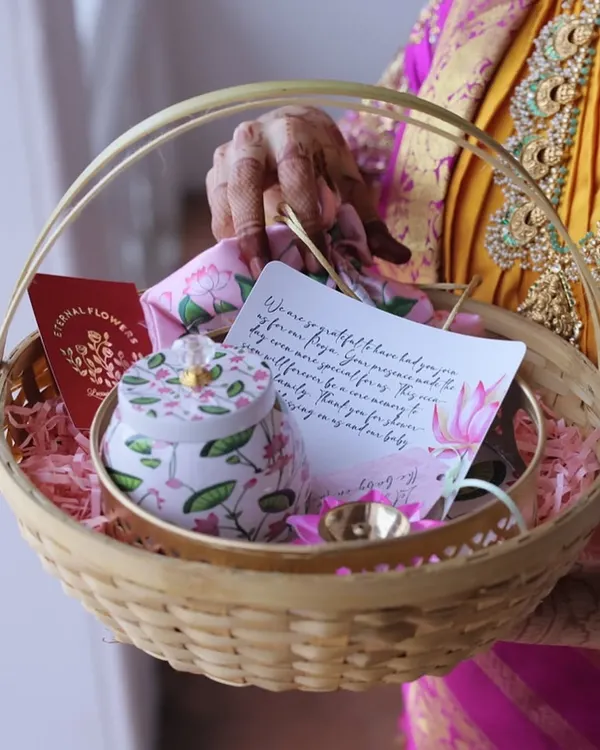A return gift basket for a 'Valakappu' (baby shower) ceremony. It includes a floral tin, a handwritten thank you note, and other small tokens of appreciation for guests.