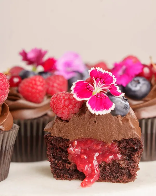 A look inside my Dark Chocolate Berry Cupcake. It’s crafted with a rich Belgian dark chocolate ganache and filled with a surprise house-made raspberry compote, all topped with fresh summer berries and edible flowers. This is an egg-free dessert that delivers pure indulgence.