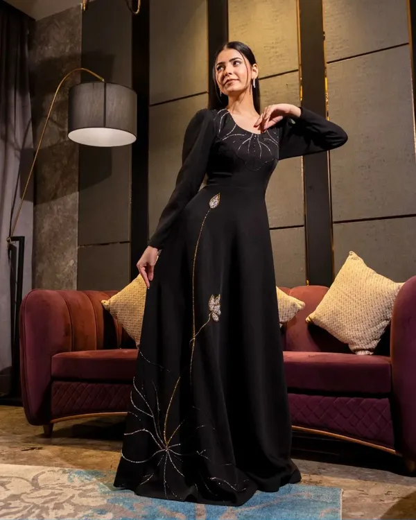 A full-length shot of a model in a black gown with delicate gold embroidery. The studio lighting is carefully placed to make the embroidery shimmer, highlighting the garment's premium quality.