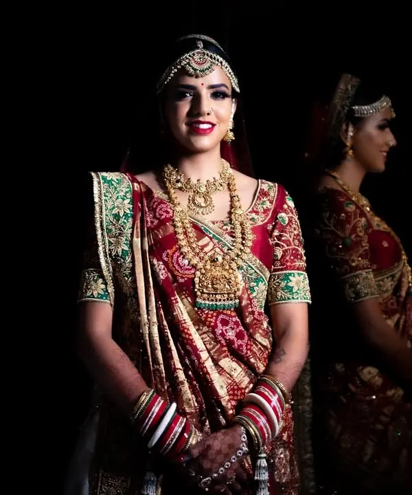 A stunning bridal portrait against a black background, with a reflection adding depth. The lighting perfectly highlights the intricate details of her traditional attire and jewelry.
