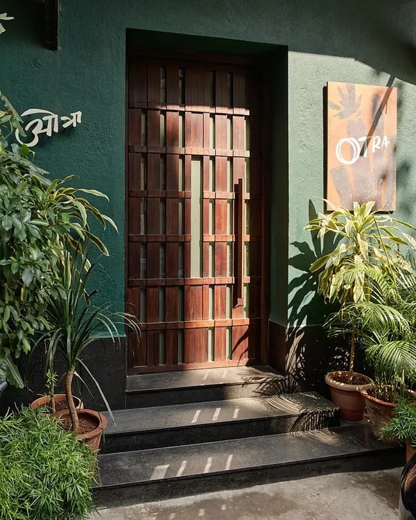 The entrance to Otra restaurant in Mumbai's historic Kala Ghoda district. The deep green facade and custom-designed wooden door create an intriguing first impression, hinting at the unique dining experience that lies within.