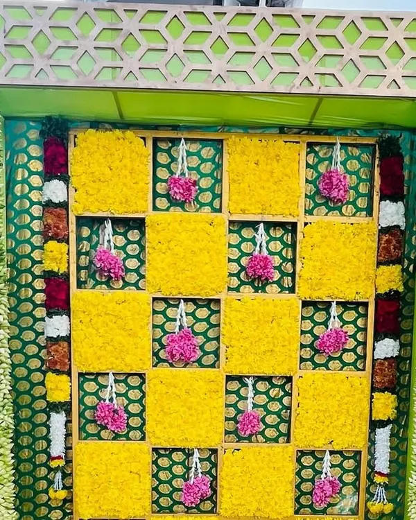 A close-up of a Haldi backdrop, showing the checkerboard pattern of yellow marigolds and hanging pink floral tassels. The intricate design adds a beautiful texture to the decor.
