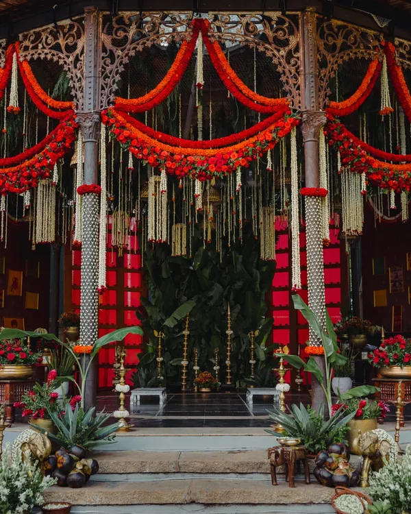 This mandap design is a tribute to South Indian royalty. The bold red backdrop, framed by traditional pillars and adorned with marigold and tuberose garlands, creates a space that is both grand and deeply rooted in heritage for the main wedding ceremony.