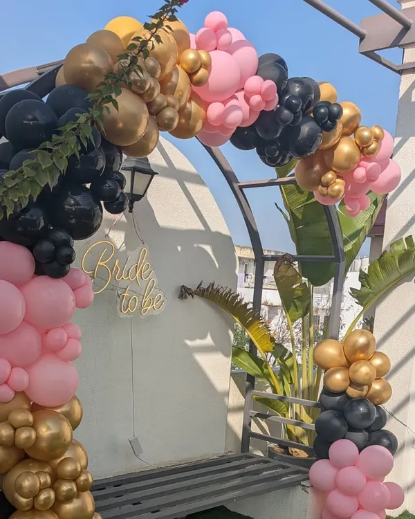 A chic and modern balloon arch in black, pink, and gold for a stylish 'Bride to be' terrace party. This setup is perfect for outdoor bachelorette celebrations.