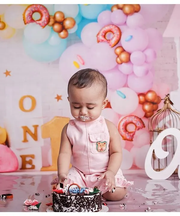 A little boy enjoys his first birthday cake during a cakesmash session. The setup includes pastel balloons and "ONE" signs, creating a perfect scene for a milestone celebration.