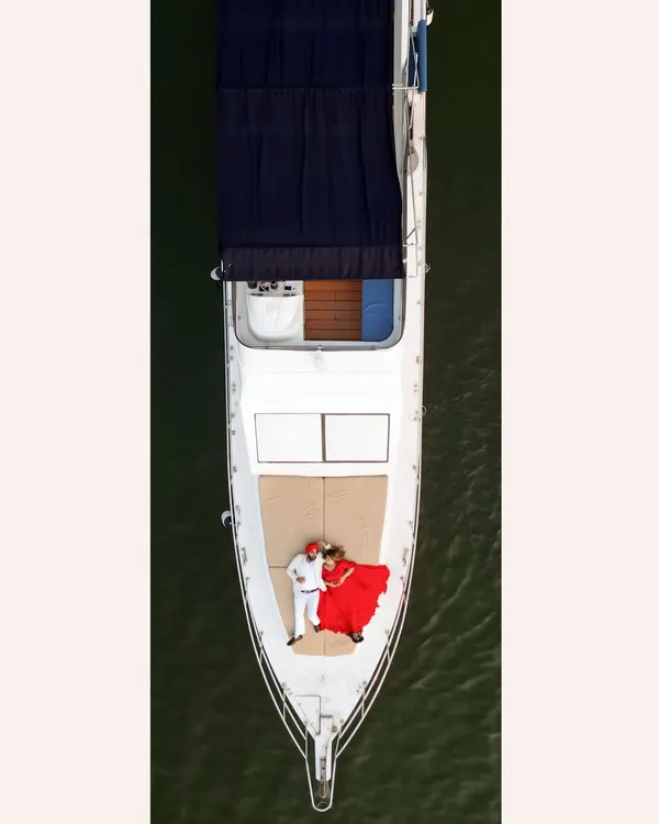 An epic aerial drone shot of Gurneet and Gurbani on a yacht in Goa. The bride's flowing red dress against the green sea creates a stunning, cinematic visual.