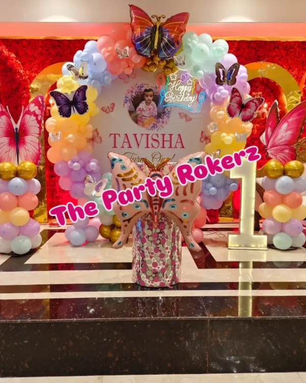 Here is the full view of a beautiful butterfly-themed first birthday I did. The setup includes a circular backdrop with the baby's name, a pastel balloon arch, large butterfly foils, and a light-up marquee number.