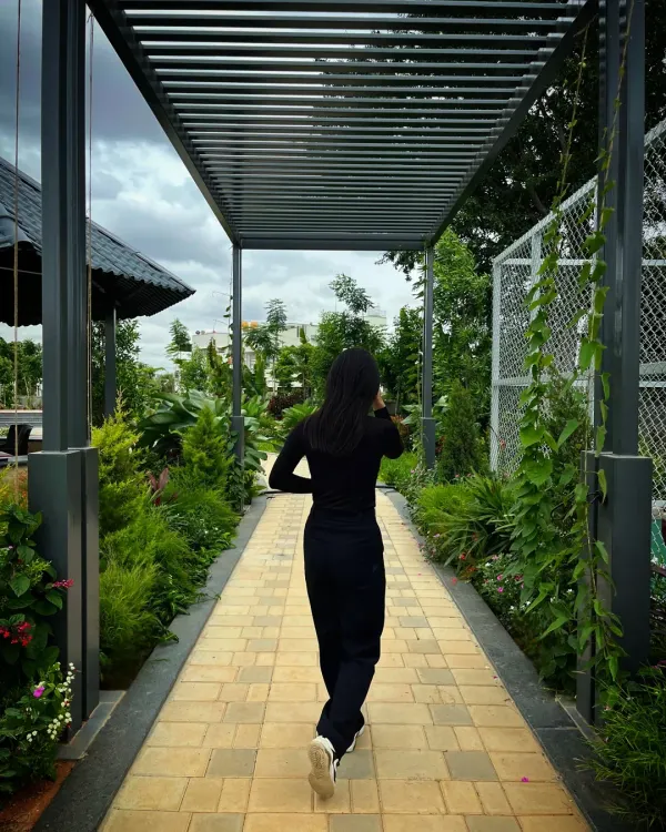 A modern pergola creates a shaded walkway at Serene Exotica, with its clean lines guiding movement while framing views of the lush gardens on either side.
