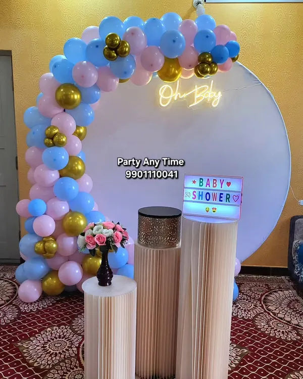 An "Oh Baby" decoration for a baby shower, with a pink, blue, and gold balloon arch against a white circular backdrop.