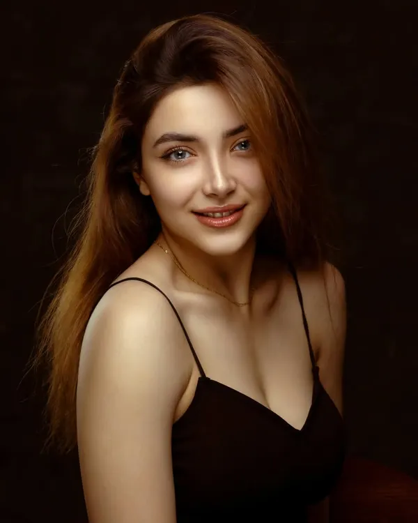 A classic beauty portrait with a warm, inviting smile. The soft lighting and simple black top put all the focus on her natural elegance and bright expression.
