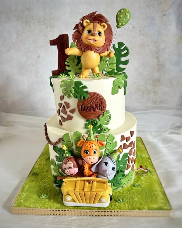 A safari cake for a roaring first birthday celebration! This two-tier design features a hand-sculpted lion topper and a jeep full of his adorable animal friends.