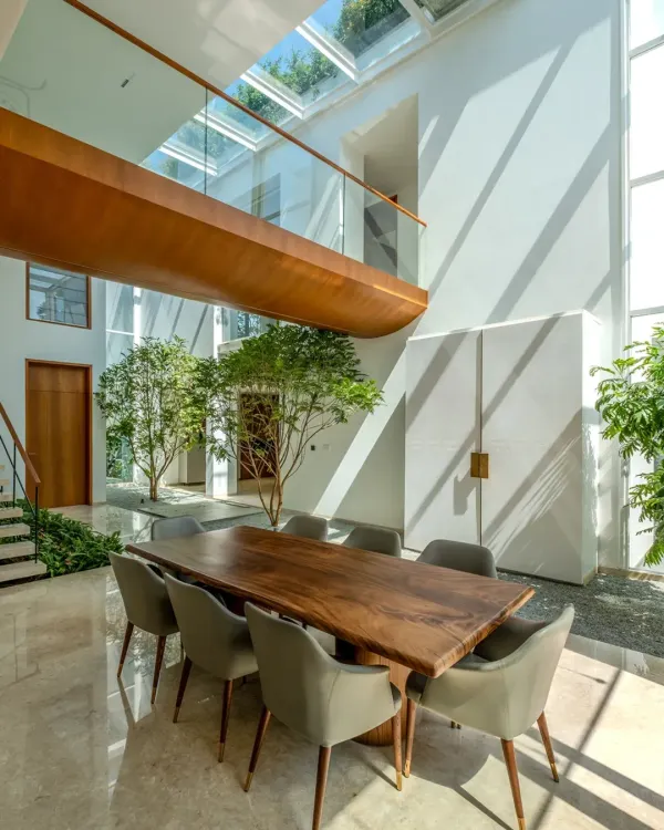 This is the heart of the Split House, where a central, double-height courtyard and a massive skylight dissolve the boundaries between indoors and out. We designed this space to be a tranquil core for family life, where the changing light marks the passing of the day. The design uses a minimal palette of marble, teak, and glass to keep the focus on the spatial volume and the connection to nature.