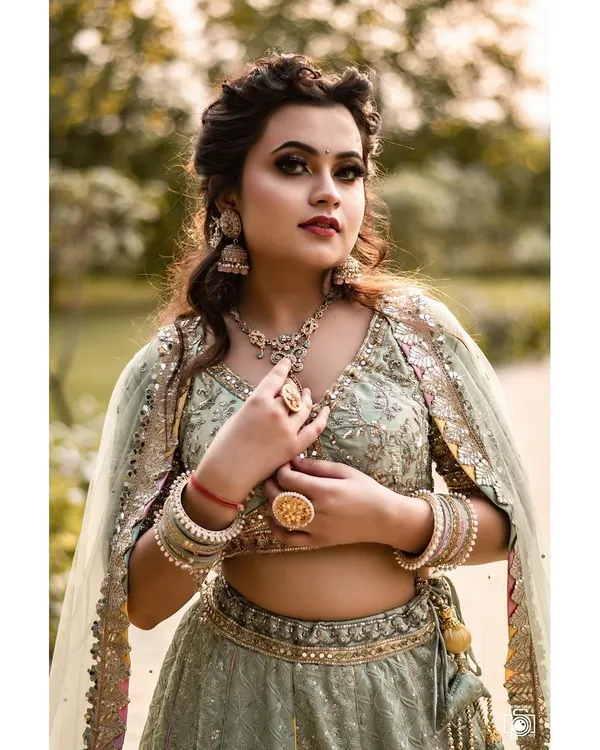This portrait captures the regal elegance of a beautifully detailed lehenga. Shot outdoors, the soft natural light complements the pastel green fabric and intricate gold jewelry, creating a look of timeless grace.