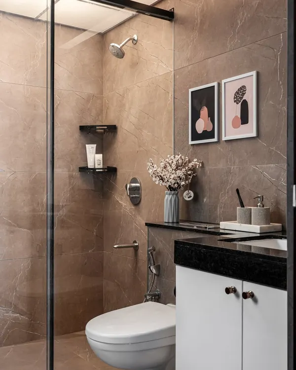 A modern and minimalist bathroom with neutral-toned marble-look tiles. The space includes a glass-partitioned shower and a compact vanity with simple, elegant decor.