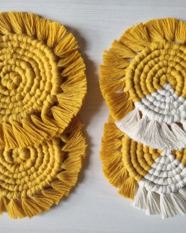A set of my round, fringed macrame coasters in a sunny yellow. This image shows two design variations, one solid and one with a white accent, perfect for protecting your surfaces with style.