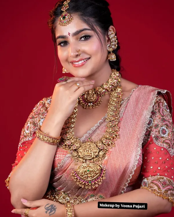 A classic South Indian bridal portrait. This look features a flawless matte base, beautifully defined eyes, and traditional temple jewelry against a vibrant red backdrop, capturing the pure essence of a muhoortham bride.