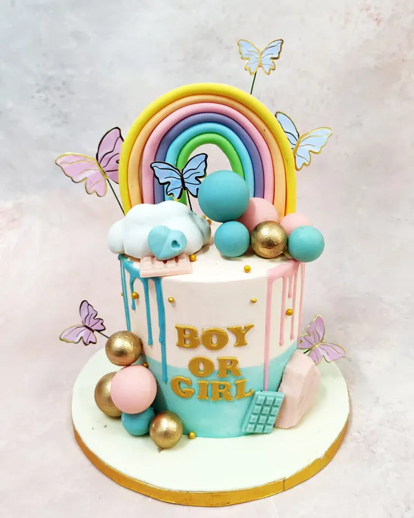 This "Boy or Girl" gender reveal cake is a whimsical masterpiece, featuring pink and blue drips, a pastel rainbow, and fluttering butterflies.