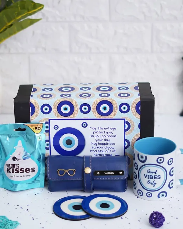 Send good vibes with this complete Evil Eye Hamper. It includes a themed ceramic mug, two matching tea coasters, a personalized eyewear case, and Hershey's chocolates, all packed in an evil eye themed box.