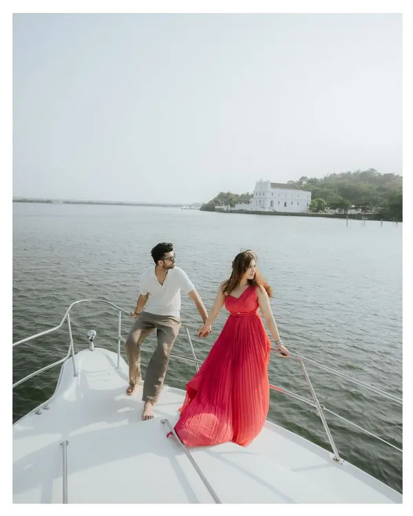 A vibrant, joyful shot of a couple on a yacht in Goa. The bride's bright pink dress flows in the wind as they hold hands, creating a picture of luxury and carefree romance on the water.