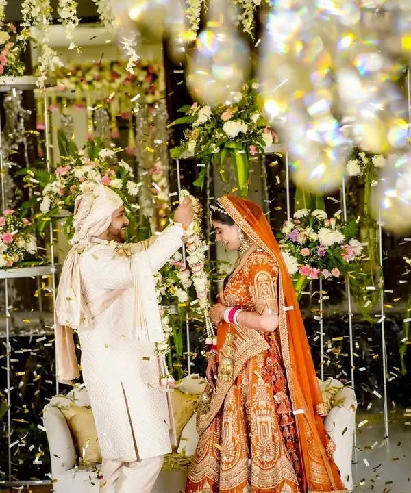 The magical moment of the varmala exchange, framed by a stunning floral and crystal backdrop with confetti falling all around. This is a classic wedding shot captured with a sense of grandeur.