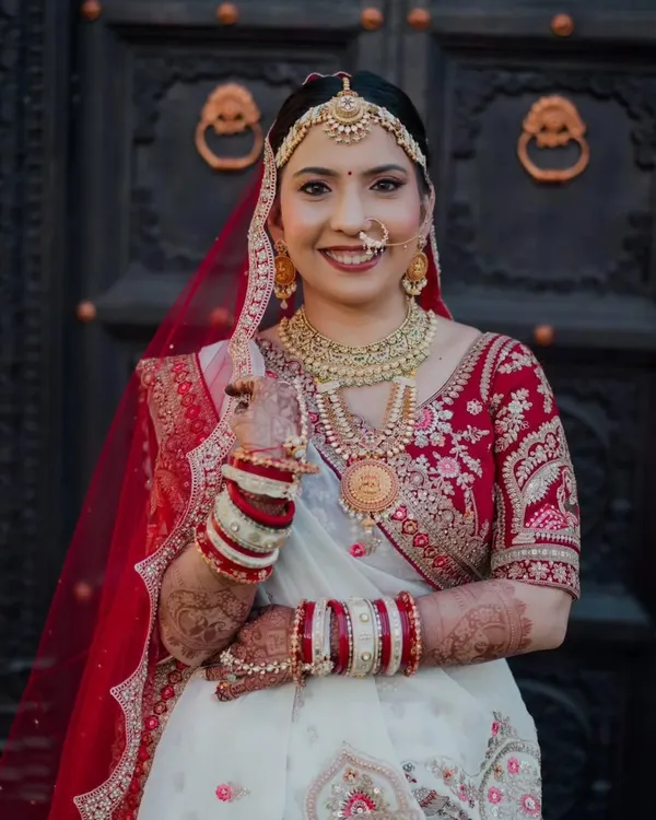 This bride looks absolutely regal in her red and white embroidered lehenga. Her makeup features a classic red lip and defined eyes, a timeless combination that perfectly complements her traditional bridal jewelry and the grandeur of her outfit.