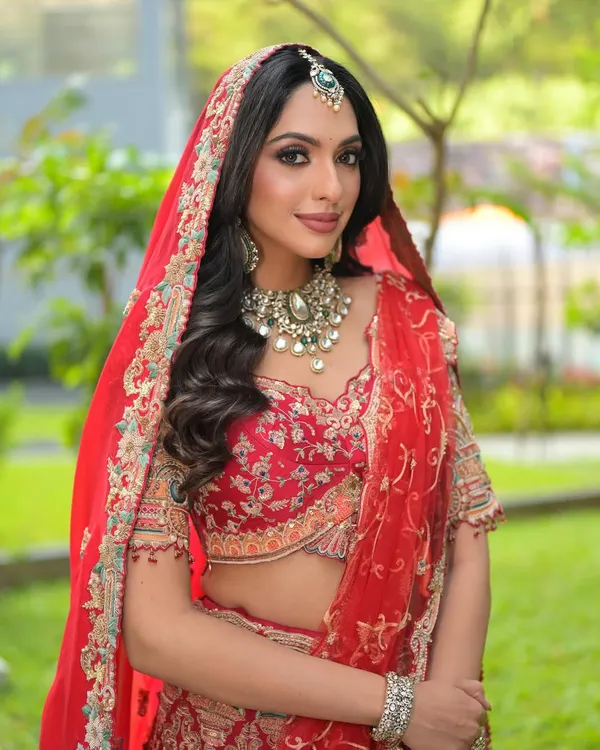 A full-length view of my signature red bridal lehenga look. The makeup is designed to be radiant in natural light, with soft, wavy hair and a perfectly draped dupatta creating a look of timeless elegance.