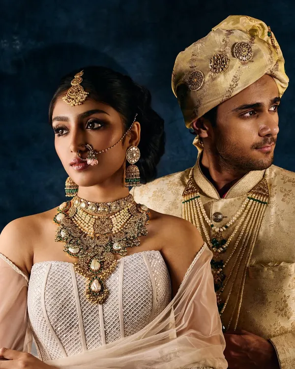 A classic couple portrait from a bridal jewellery campaign. The lighting is carefully balanced to illuminate the bride's layered necklace and maang tikka, as well as the groom's complementary jewels, creating a cohesive and luxurious look.