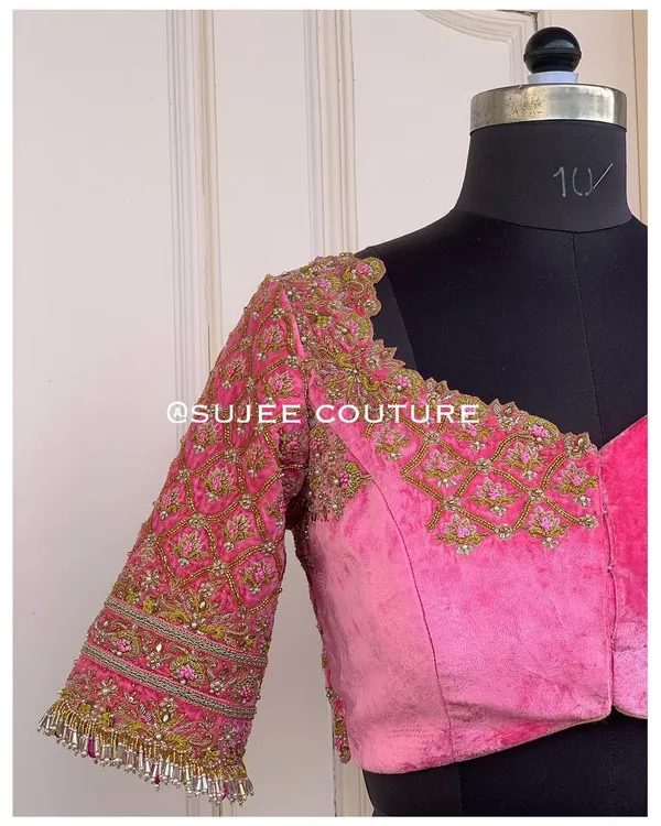 This pink velvet blouse features a sweetheart neckline and heavily embroidered sleeves. The design combines traditional zardozi patterns with a modern cut for a unique bridal piece.