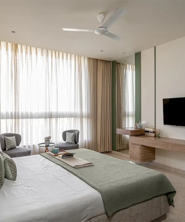 A full view of a master bedroom I furnished in a Thane apartment. I built the bed with its faux leather headboard, the floating media unit, and the small seating area with two chairs, creating a complete and cohesive look.