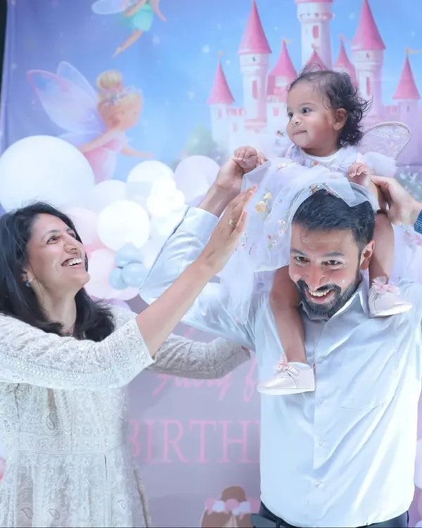 The pure joy of a birthday party! A father lifts his daughter onto his shoulders against a festive fairy-themed backdrop.