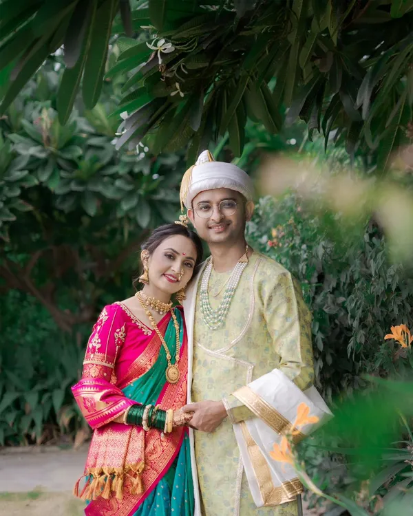 A lovely portrait of a Maharashtrian couple, their colorful traditional attire vibrant against the lush green background of their outdoor wedding.