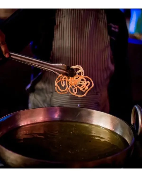 A chef carefully lifts a freshly fried, crispy nano jalebi from the hot oil. Our live jalebi station is a sensory delight, filling the air with a sweet aroma and serving this Indian classic at its absolute best.