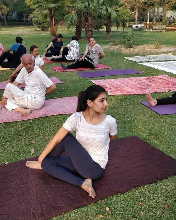 A participant holds a spinal twist during our International Yoga Day 2019 celebration in a Noida park. You can see people of all ages practicing together in the background.