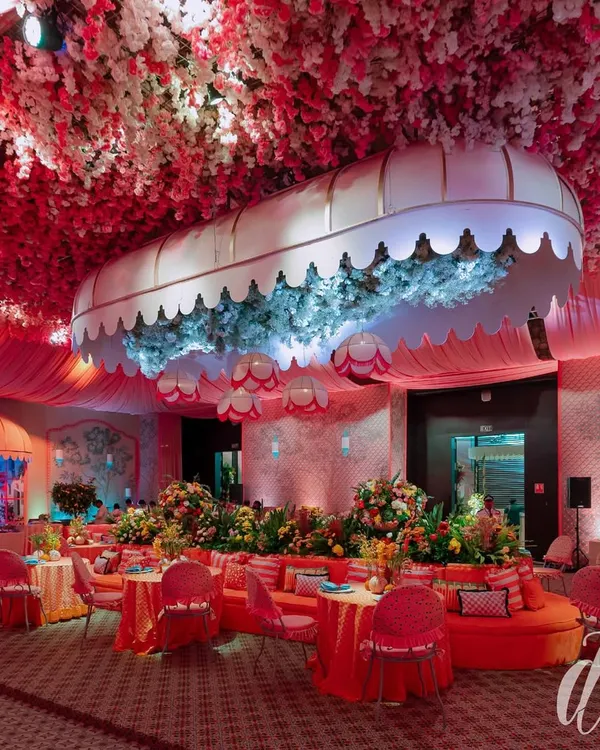 The evening look of our 'La Dolce Vita' theme, where the space was transformed with dramatic pink lighting. A custom canopy filled with blue hydrangeas became a central feature, surrounded by plush orange seating and tables set for a luxurious dinner.