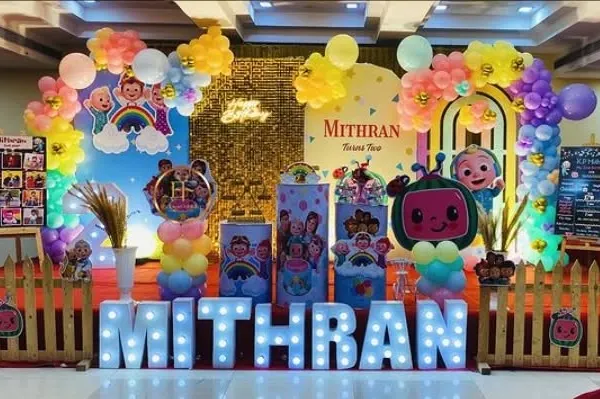 A vibrant Cocomelon themed birthday party with a large backdrop, character cutouts, and a shimmer wall for extra sparkle.