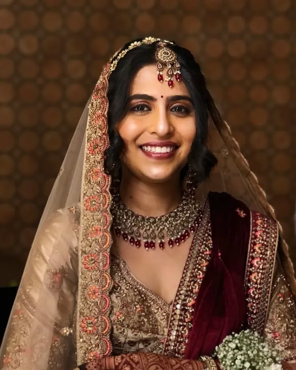 A radiant bride, her smile as bright as her stunning wedding lehenga. We created a classic bridal makeup look with defined eyes and a warm lip, paired with a soft, elegant hairstyle to complete her special day ensemble.