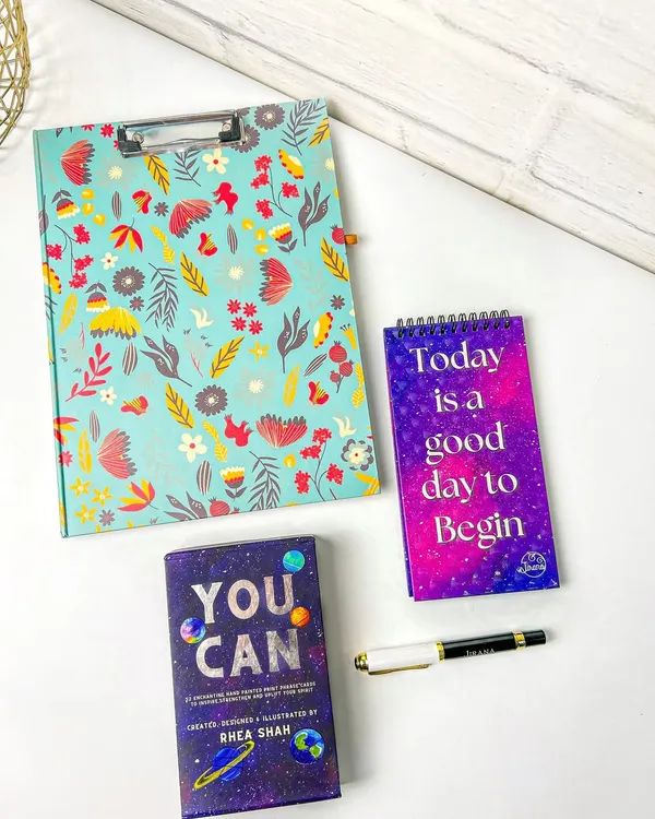 A styled flatlay of a floral clipboard, a 'You Can' card deck, and a motivational notepad. This composition is perfect for a stationery brand's social media or website.
